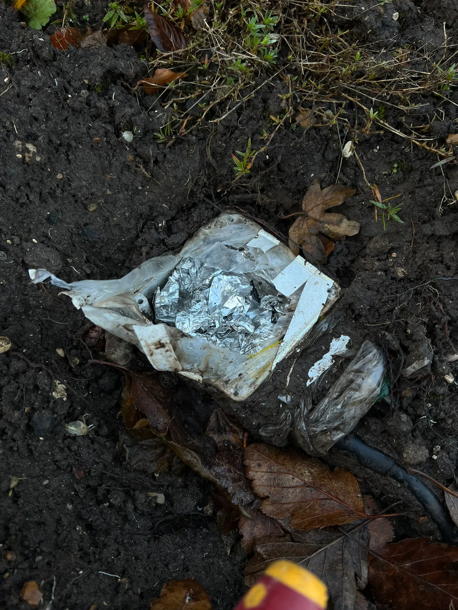 White box in garden soil with plastic wrapping, foil and a cable beside it