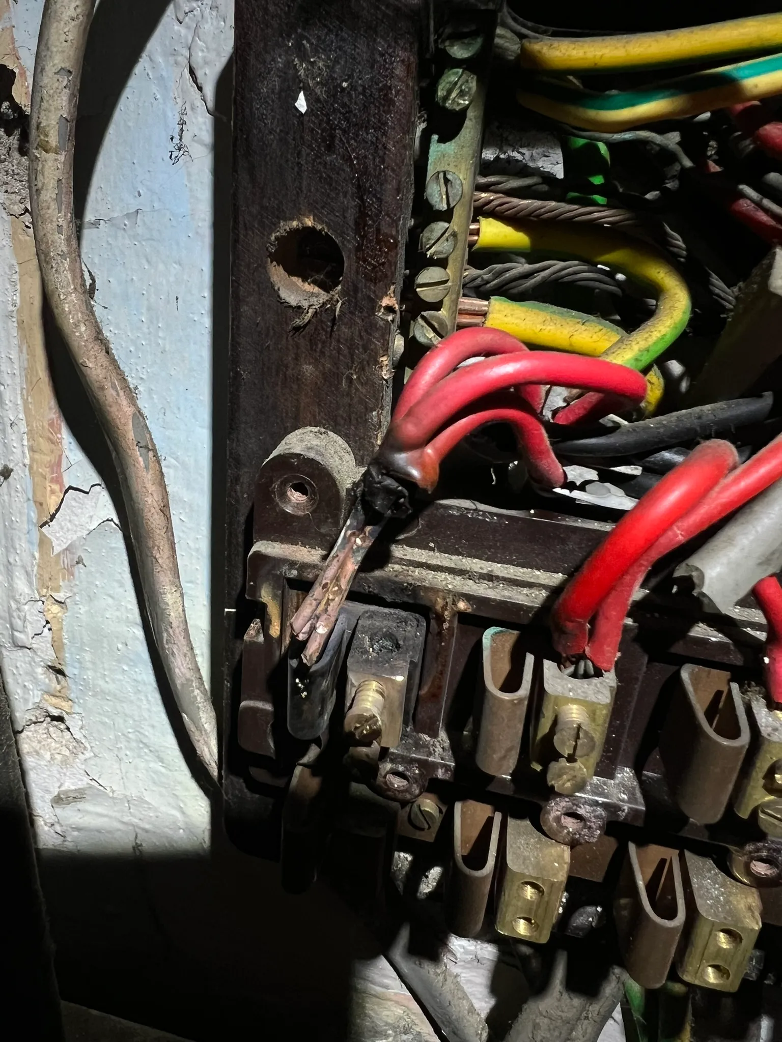 Inside an old rewireable fuse board, a clump of red conductors with burnt insulation and exposed copper beside the fuse terminals