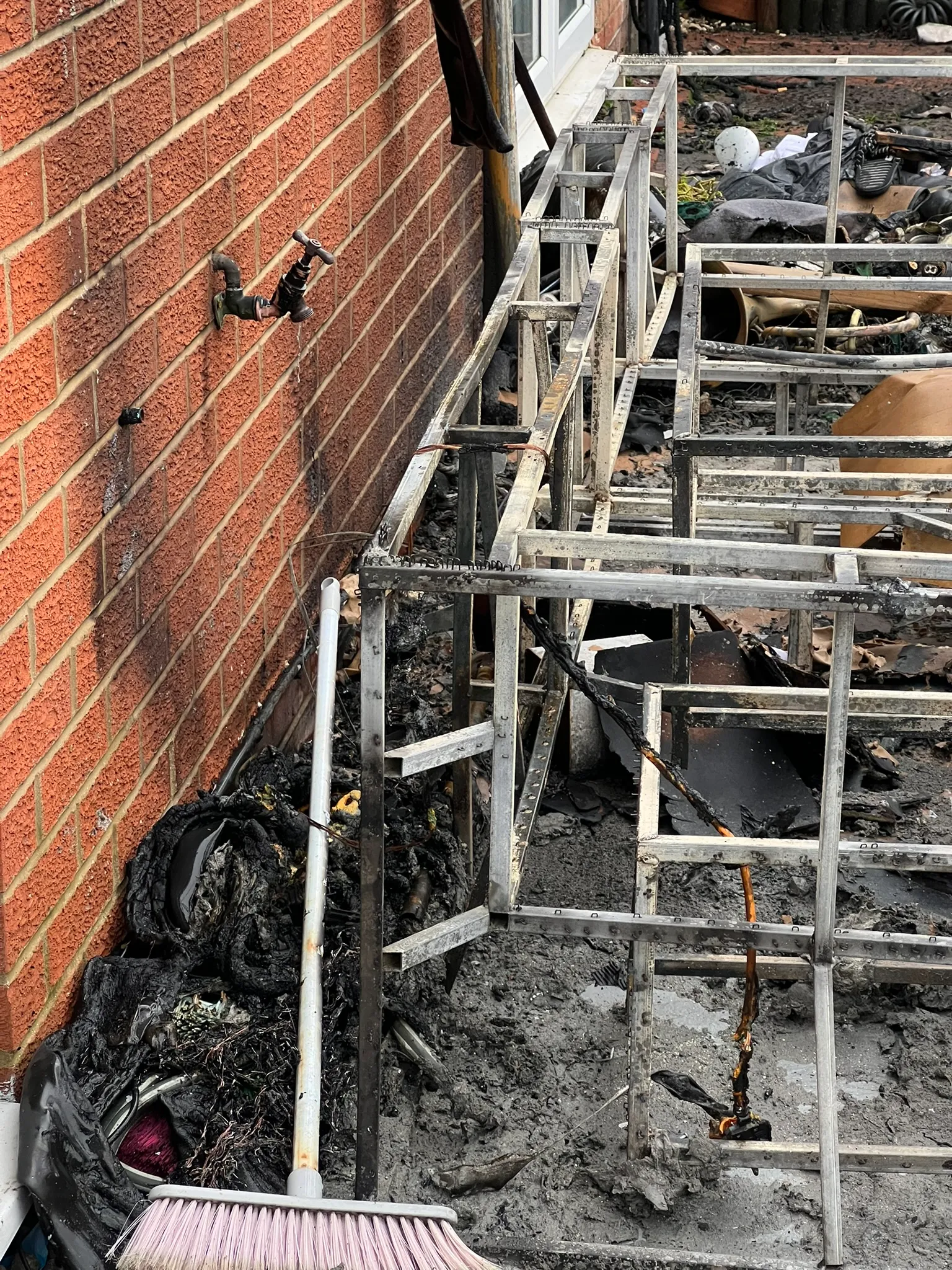 Burnt remains and exposed furniture frames beside a brick wall