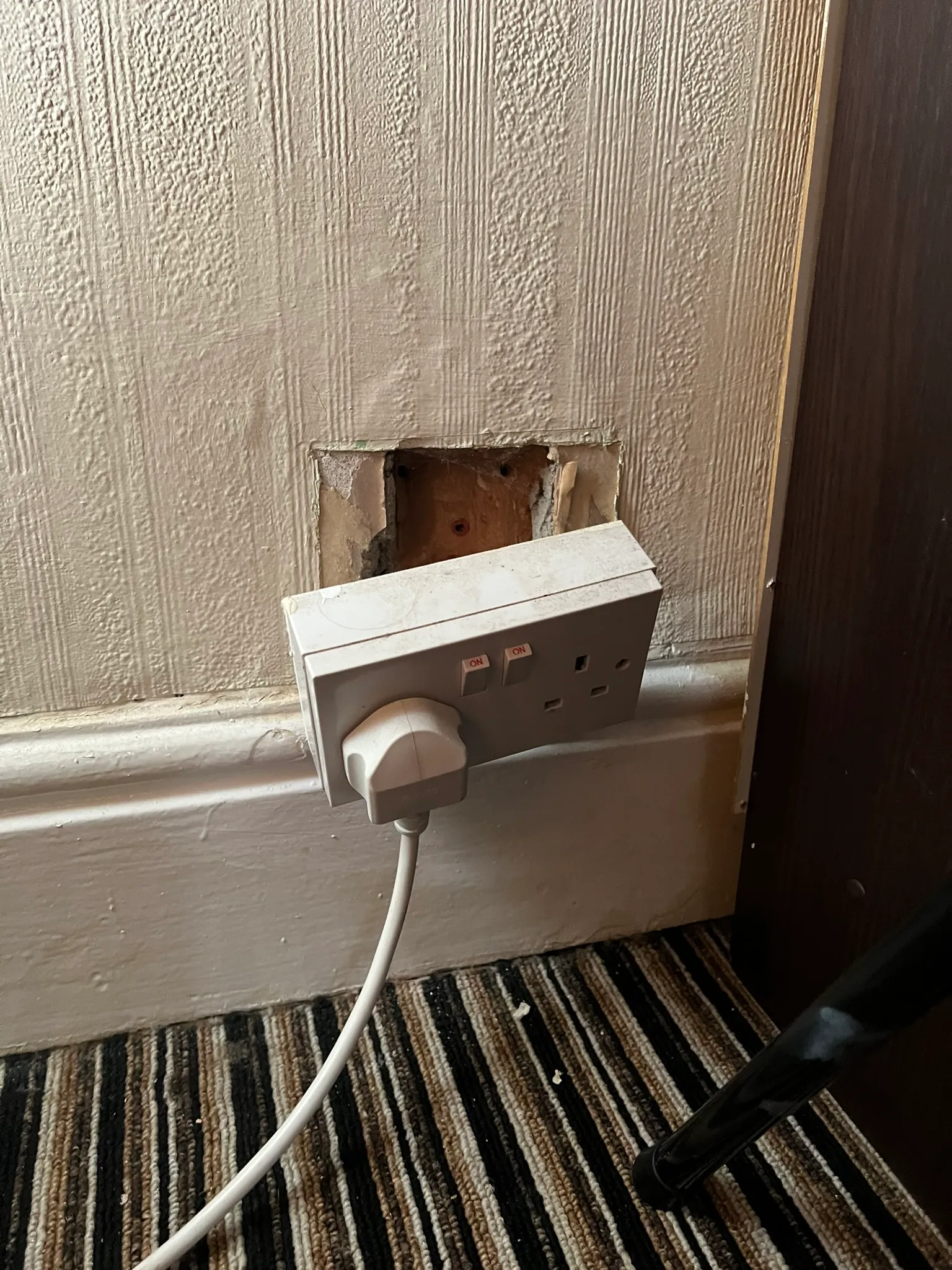 Double socket hanging away from its wall opening with a plug still inserted