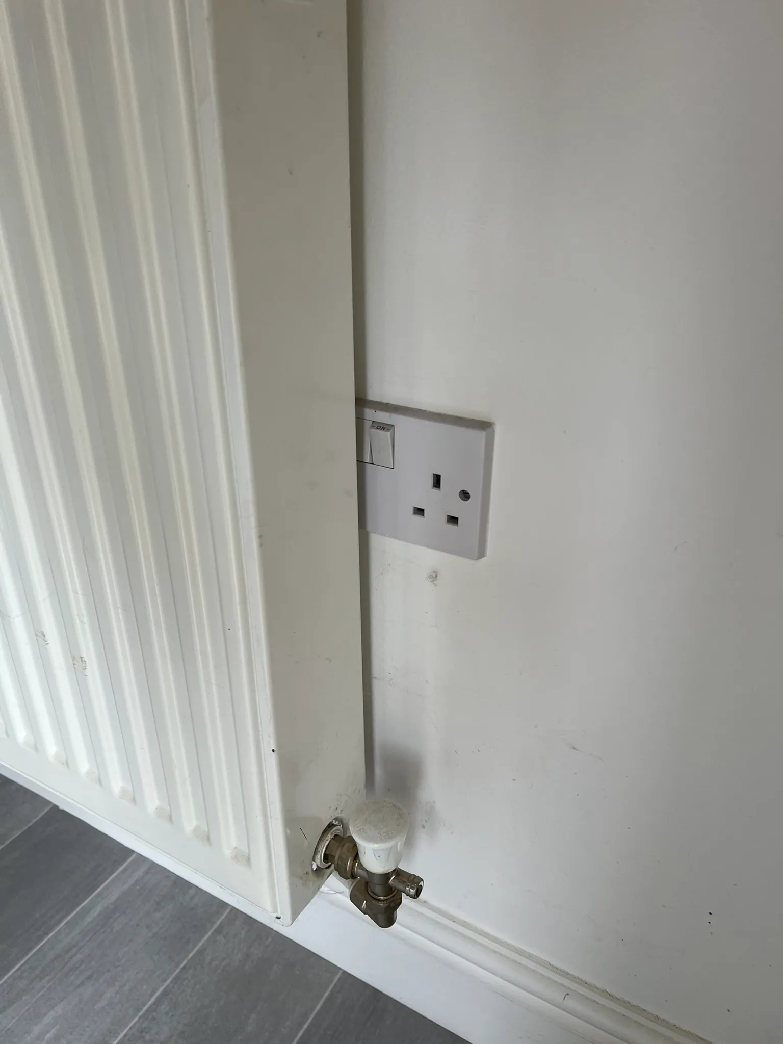 Single socket on a wall with a radiator overlapping its switch side