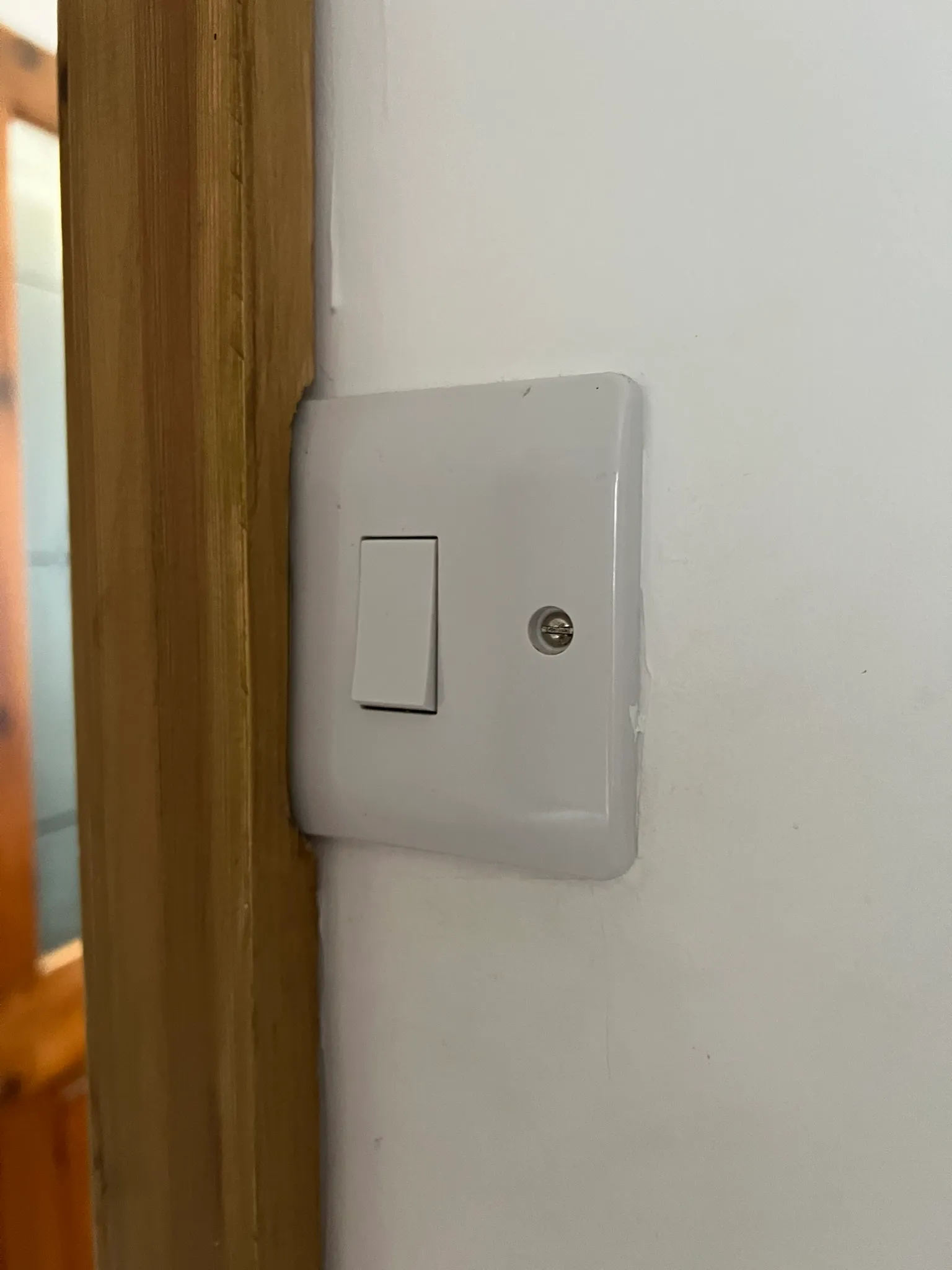 Light switch with its left edge and fixing position covered by wooden door trim