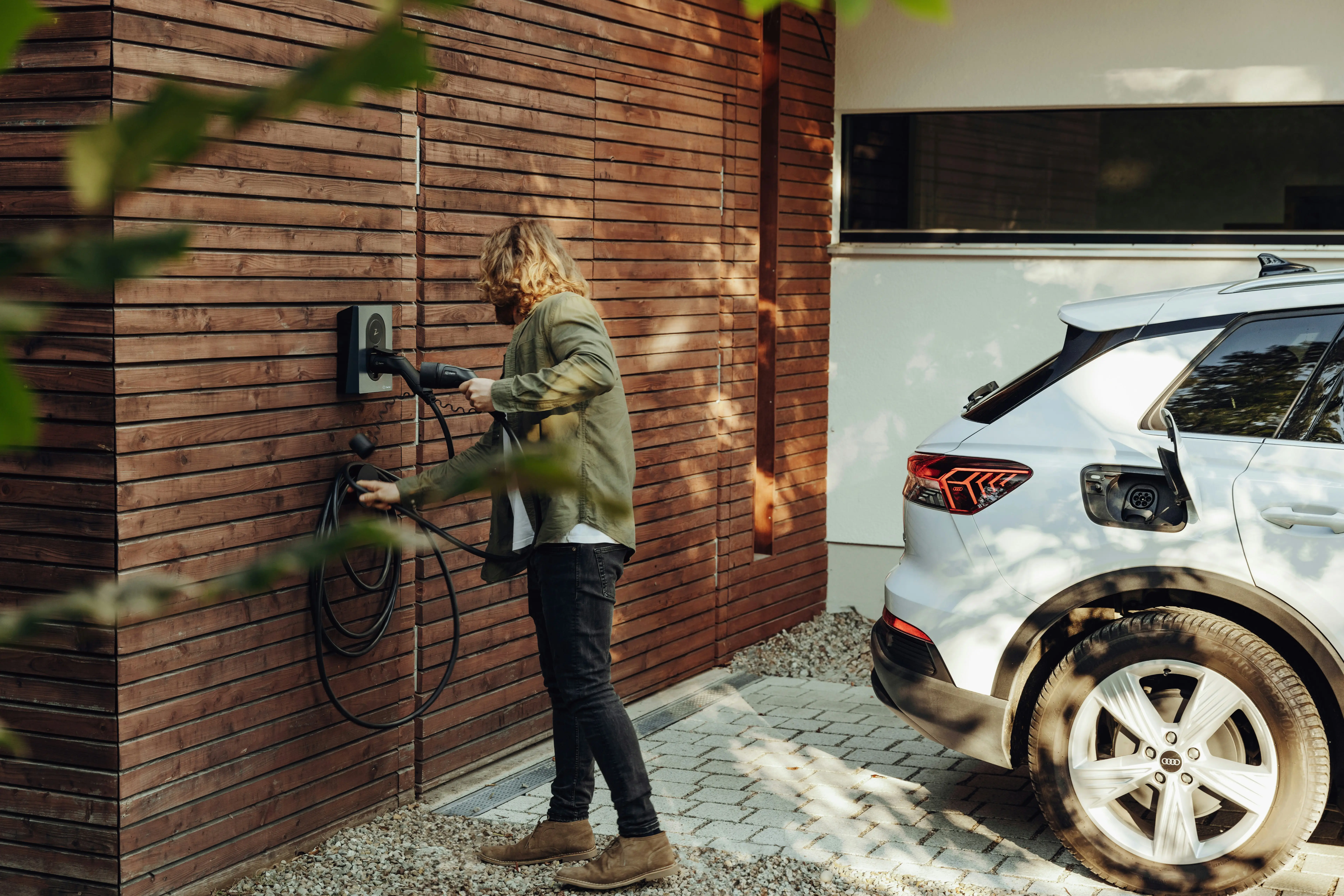 Person using a wall-mounted Zaptec charger beside a parked electric car